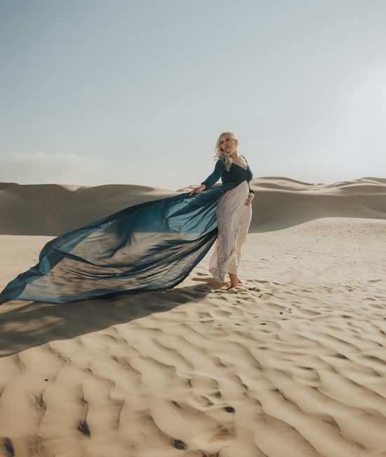 Woman in a blue flowy dress looking ethereal in the sand dunes